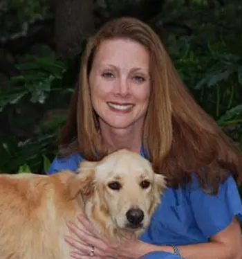 A woman holding her dog in front of some trees.