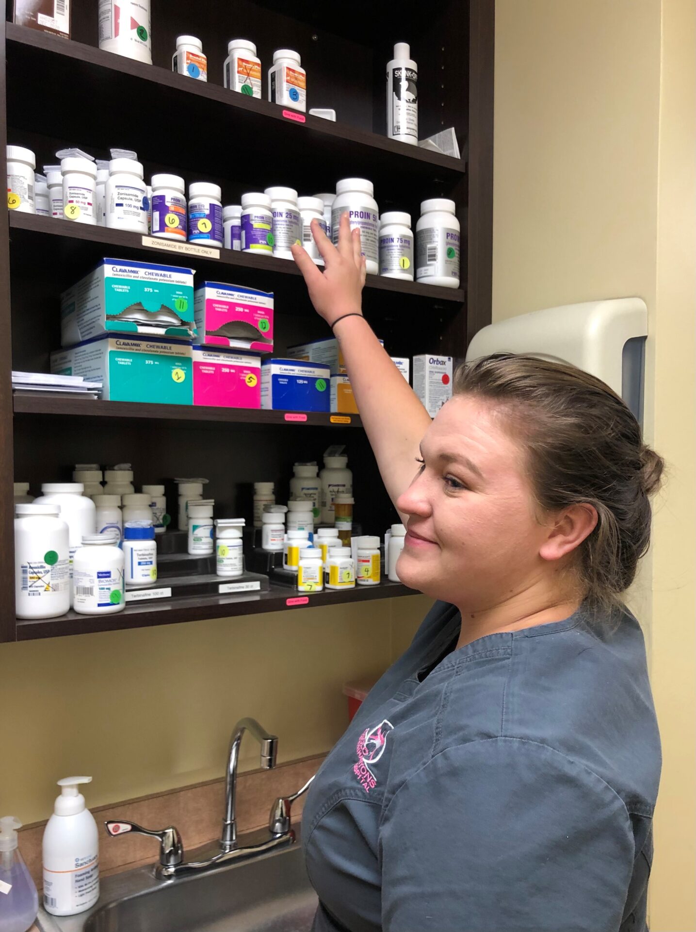 A woman in blue scrubs is reaching for some pills.