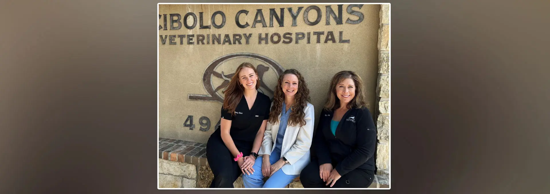 Three women standing in front of a sign for the bolo canyons veterinary hospital.