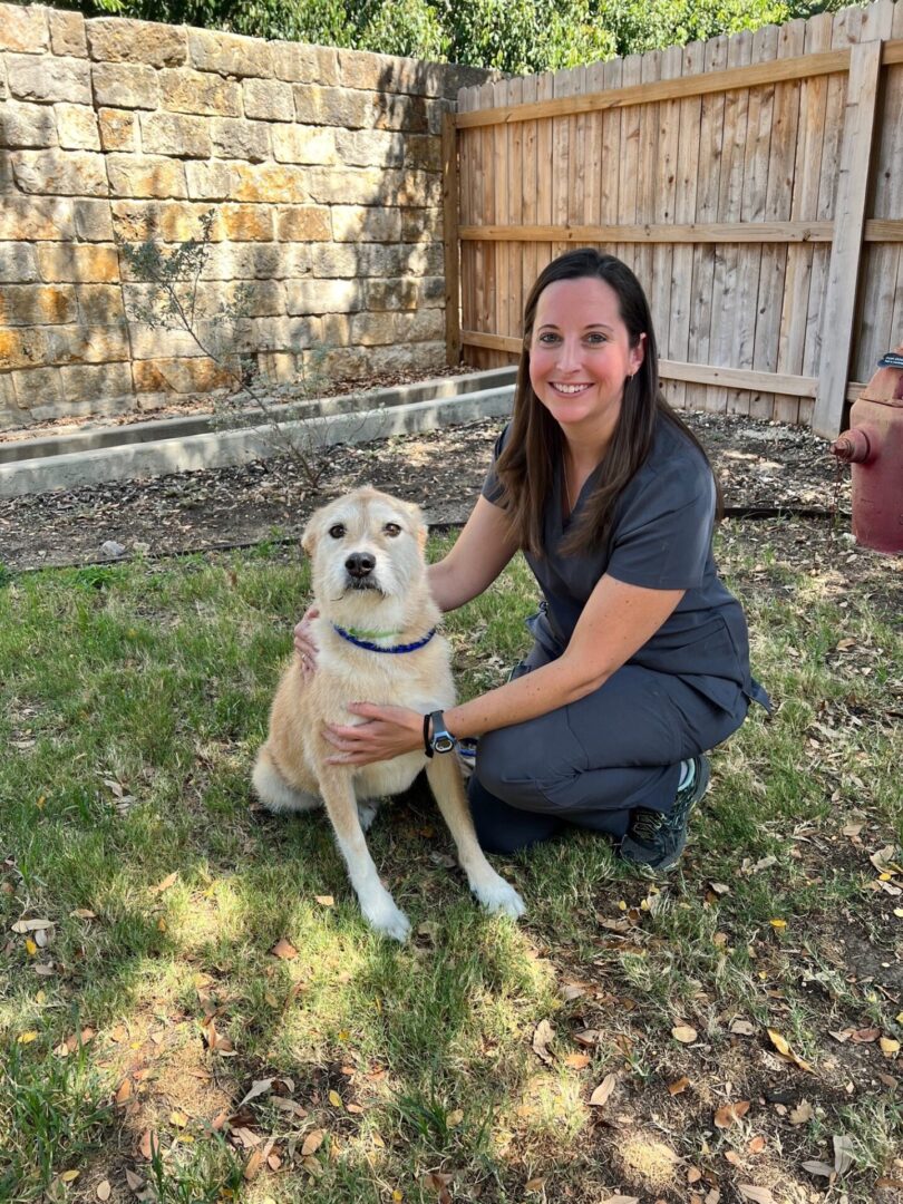 A woman kneeling down next to a dog.